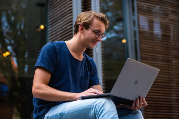 Junger Mann sitzt drau&szlig;en auf einer Treppe und arbeitet am Laptop